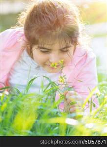 Portrait of a little girl enjoying flower aroma, having fun on fresh green grass field in spring sunny day, cute child with pleasure spending time outdoors