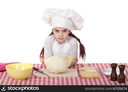 Portrait of a little girl in a white apron and chefs hat shred cabbage in the kitchen, isolated on white background