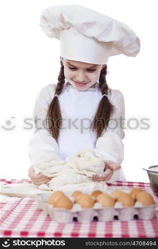 Portrait of a little girl in a white apron and chefs hat knead the dough in the kitchen, isolated on a white background