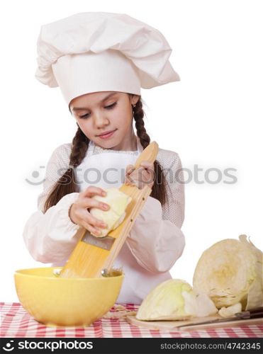Portrait of a little girl in a white apron and chefs hat shred cabbage in the kitchen, isolated on white background