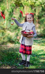 Portrait of a little girl near the Christmas tree. Girl decorates a Christmas tree in the forest with Christmas balls. Winter holidays and people concept. Merry Christmas and happy holidays.. Portrait of a little girl near the Christmas tree. Girl decorates a Christmas tree in the forest