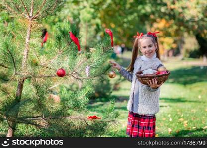 Portrait of a little girl near the Christmas tree. Girl decorates a Christmas tree in the forest with Christmas balls. Winter holidays and people concept. Merry Christmas and happy holidays.. Portrait of a little girl near the Christmas tree. Girl decorates a Christmas tree in the forest with Christmas balls.