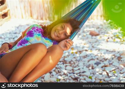 Portrait of a little girl on summer holidays, swinging in hammock on the beach, with pleasure spending time in summer camp near the sea, enjoying happy active vacation