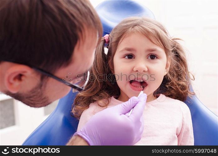 Portrait of a little girl that is sitting with his open mouth and checks the teeth at the dentist. The reception at the dentist