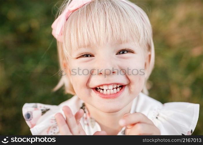 Portrait of a little laughing beautiful girl on nature on summer day vacation. child in dress is playing in the green park at the sunny time. The concept of family holiday and time together.. Portrait of a little laughing beautiful girl on nature on summer day vacation. child in dress is playing in the green park at the sunny time. The concept of family holiday and time together