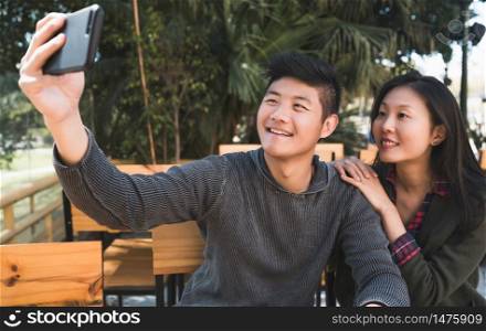 Portrait of a lovely asian couple having good time and taking a selfie with mobile phone in coffee shop.