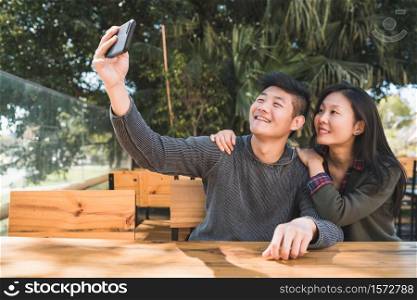 Portrait of a lovely asian couple having good time and taking a selfie with mobile phone in coffee shop.