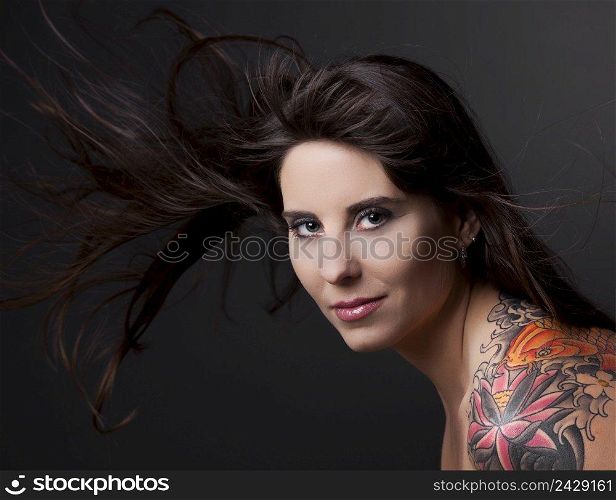 Portrait of a lovely woman with a tatto on the shoulder against a grey background and spread hair