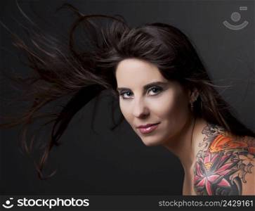 Portrait of a lovely woman with a tatto on the shoulder against a grey background and spread hair