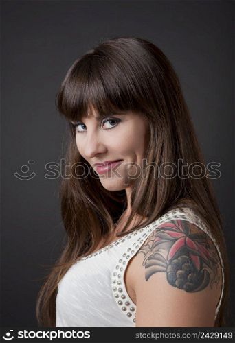 Portrait of a lovely woman with a tatto on the shoulder against a grey background 