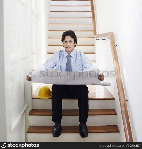 Portrait of a male architect holding blueprints on a staircase