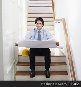 Portrait of a male architect holding blueprints on a staircase