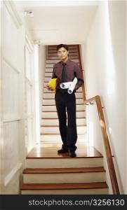 Portrait of a male architect holding rolled up blueprints and a hardhat on a staircase