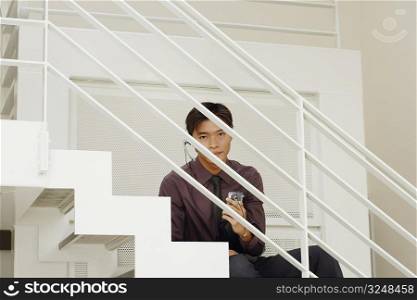 Portrait of a male customer service representative sitting and holding a mobile phone on the staircase