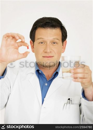 Portrait of a male doctor holding a glass of water and a capsule