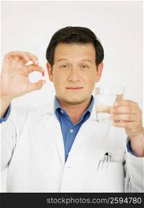 Portrait of a male doctor holding a glass of water and a capsule