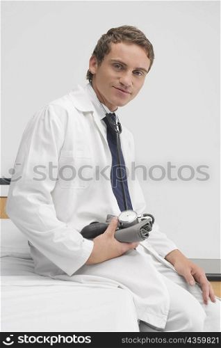 Portrait of a male doctor sitting on the bed and holding a blood pressure gauge