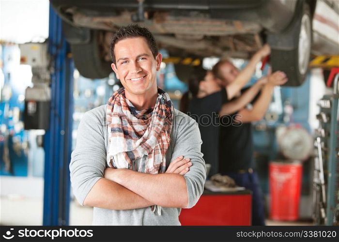 Portrait of a male happy customer in an auto repair shop with mechanics in background