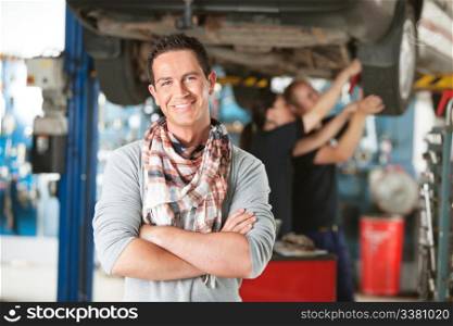 Portrait of a male happy customer in an auto repair shop with mechanics in background