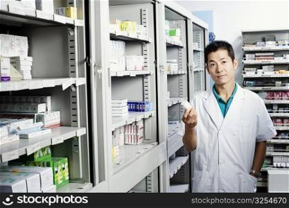 Portrait of a male pharmacist holding a bottle in a store room