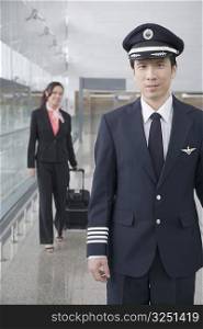 Portrait of a male pilot with a female cabin crew walking behind him