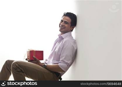 Portrait of a man holding a gift leaning against wall