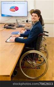 Portrait of a man in a wheelchair participating in a meeting with colleagues in office environment with a digital screen, might be a startup company