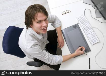 Portrait of a man sitting behin a desk with keyboard, graphic tablet and monitor in an office