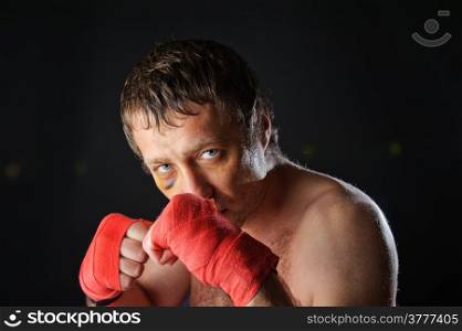 Portrait of a man with a bruise in a battle position. Clenched fists. Dark background.