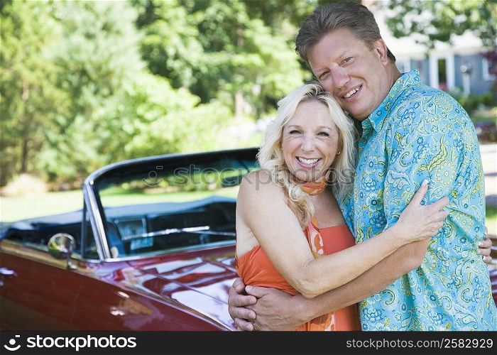 Portrait of a mature couple embracing each other and smiling in front of a convertible car