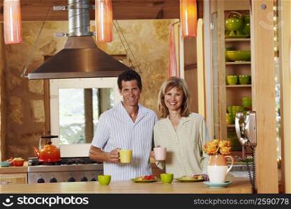 Portrait of a mature couple holding cups in a kitchen and smiling