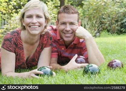 Portrait of a mature couple lying on grass and holding balls