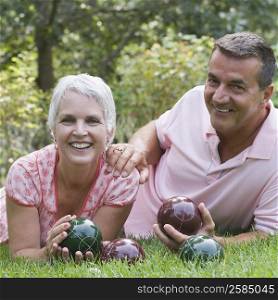 Portrait of a mature couple lying on grass and holding bocce balls