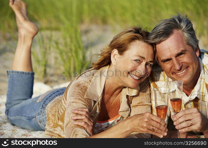 Portrait of a mature couple lying on the beach and holding champagne flutes