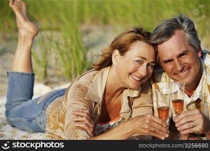 Portrait of a mature couple lying on the beach and holding champagne flutes
