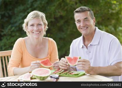 Portrait of a mature couple sitting at a table and holding slices of watermelon