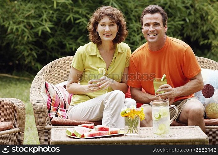 Portrait of a mature couple sitting on a couch and holding glasses of lemonade