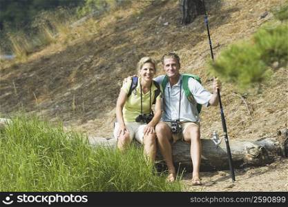 Portrait of a mature couple sitting on a tree trunk in a forest and smiling