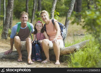 Portrait of a mature couple sitting on a tree trunk with their daughter in a forest