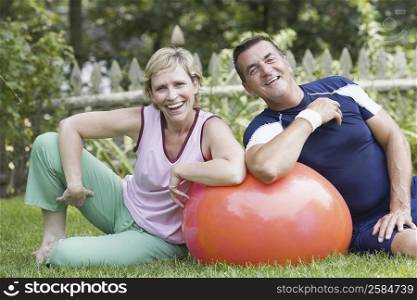 Portrait of a mature couple sitting on grass with a fitness ball