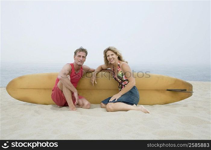 Portrait of a mature couple sitting on the beach with a surfboard