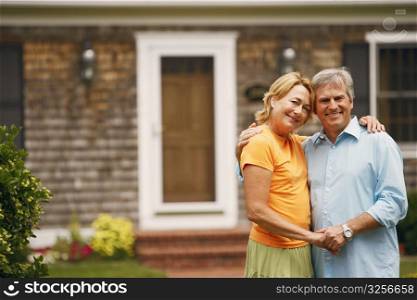 Portrait of a mature couple standing with their arms around each other in front of a house