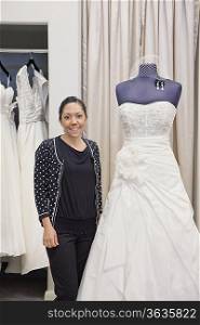 Portrait of a mature employee standing by elegant wedding dress in bridal store