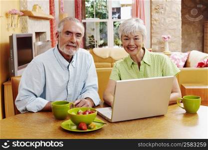 Portrait of a mature man and a senior woman sitting in front of a laptop and smiling