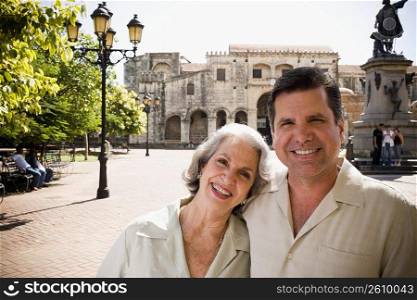 Portrait of a mature man and his mother smiling in front of a statue, Santo Domingo, Dominican Republic