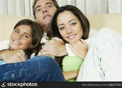 Portrait of a mature man and his two daughters sitting on a couch and smiling