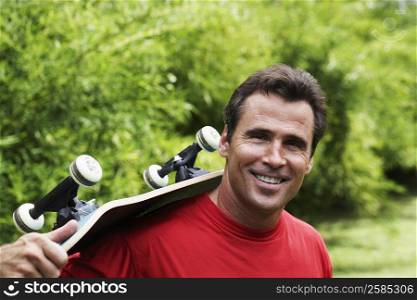 Portrait of a mature man carrying a skateboard on his shoulder and smiling