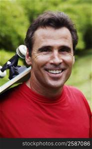 Portrait of a mature man carrying a skateboard on his shoulder and smiling