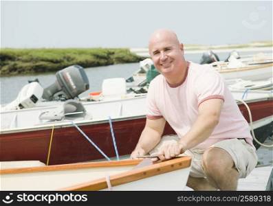 Portrait of a mature man crouching and smiling near a motorboat
