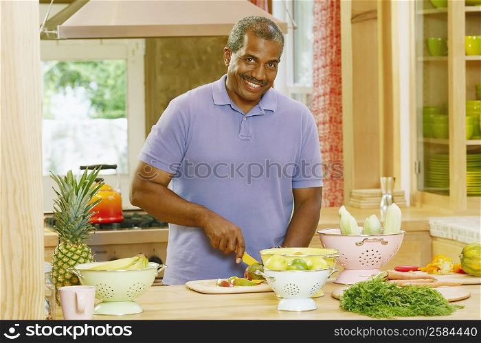 Portrait of a mature man cutting vegetables in a kitchen and smiling